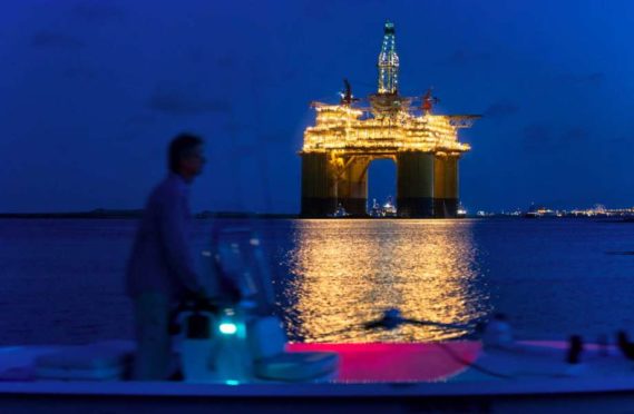 A boater passes the Royal Dutch Shell Plc Olympus tension leg platform (TLP) at dawn as it sets sail from Kiewit Offshore Services in Ingleside, Texas, U.S., on Saturday, July 13, 2013. Olympus, Shell's biggest constructed tension leg platform, started the ten day, 425-mile voyage to Mars B Field in the Gulf of Mexico on July 13. Photographer: Eddie Seal/Bloomberg